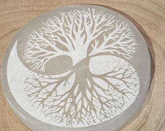 May include: A round, light-colored stone with a white tree of life design. The tree is split into two halves, resembling a Yin and Yang symbol. The stone is set on a wooden surface.