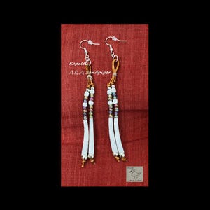 May include: A pair of long, white leather earrings with brown leather accents and multi-colored beads. The earrings are called "Kapalel" AKA "Sandpiper".