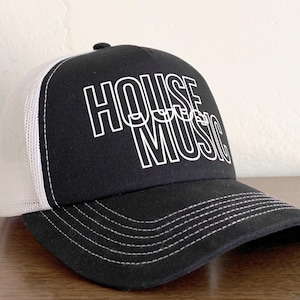 Op de afbeelding: Een zwart-witte truckerpet met een zwart voorpaneel waarop de tekst HOUSE MUSIC in witte omlijnde letters staat. De pet heeft een wit mesh achterpaneel en een zwarte klep met witte stiksels langs de rand van de klep.