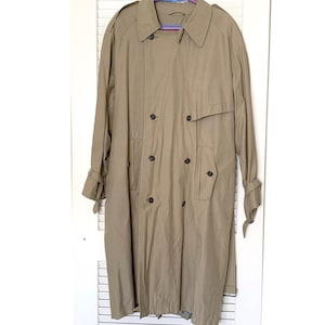 May include: A tan double-breasted trench coat with a notched collar, epaulets, and a storm flap. The coat has a button closure, side pockets, and adjustable cuffs. The coat is hanging on a hanger against a white background.