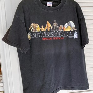 May include: Black t-shirt with a graphic of the Star Wars characters from the original trilogy. The text "Star Wars The Trilogy Special Edition" is printed in red on the shirt.
