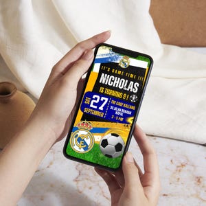 Puede incluir: Un teléfono inteligente muestra una invitación de cumpleaños con temática de fútbol. La invitación incluye el texto "IT'S GAME TIME!!! NICHOLAS IS TURNING 9!" y la fecha "27 SEPTIEMBRE". También se ven un balón de fútbol y el logotipo del equipo.