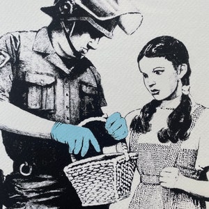 以下が含まれることがあります： ヘルメットと制服を着た警察官が、ドレスを着た女の子が持っているバスケットを調べている白黒プリント。警官は青い手袋をしています。女の子は三つ編みをしており、心配そうな表情をしています。