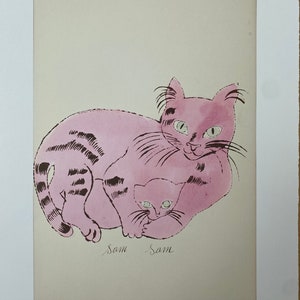 Könnte beinhalten: Rosa Druck einer Mutterkatze und eines Kätzchens mit dem Text "Sam Sam" darunter. Die Katzen haben grüne Augen und schwarze Streifen. Der Druck befindet sich auf einem cremefarbenen Hintergrund, mit der Signatur des Künstlers unten rechts.