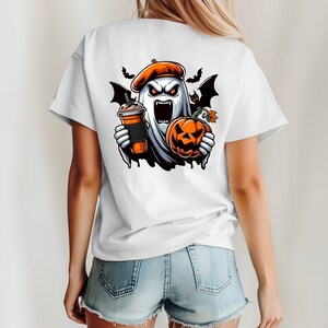 May include: White t-shirt featuring a graphic of a ghost wearing a beret, holding a pumpkin and a cup of coffee. The ghost has a scary expression with fangs and red eyes.