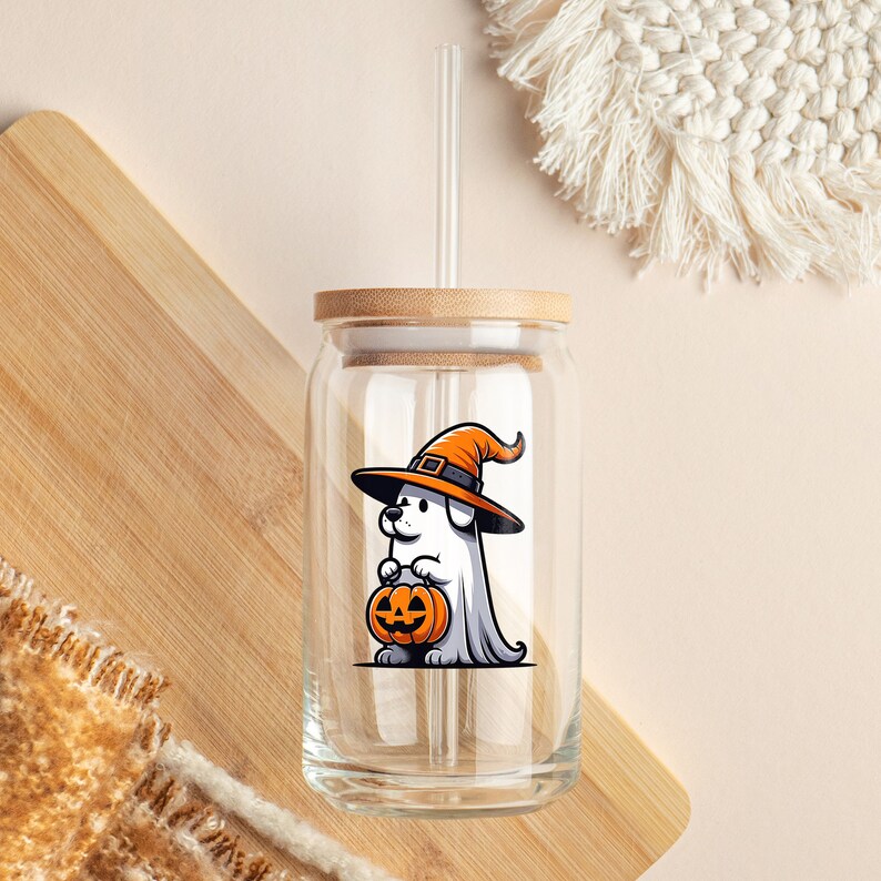 Puede incluir: Un vaso de vidrio transparente con tapa de bamb&uacute; y una pajita. El vaso tiene un perro fantasma blanco con un sombrero de bruja y sosteniendo una calabaza de Halloween.