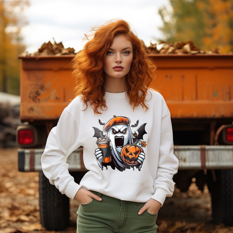 May include: A white sweatshirt featuring a graphic print of a ghost wearing a beret and holding a pumpkin and a cup of coffee. The ghost has a scary expression on its face and is wearing a beret. The sweatshirt is being worn by a person with long red hair.