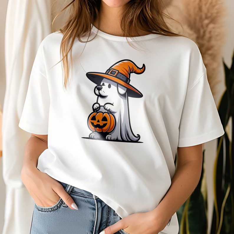 Puede incluir: Camiseta blanca con una imagen de dibujos animados de un perro con un sombrero de bruja y sosteniendo una calabaza de Halloween.