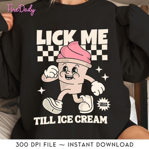 Puede incluir: Sudadera negra con un gráfico de un cono de helado de dibujos animados con un remolino rosa en la parte superior. El cono de helado lleva una sonrisa y tiene brazos y piernas. El texto "Lick Me Till Ice Cream" está impreso en la sudadera.
