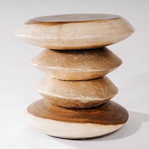 Könnte beinhalten: Ein gestapelter Beistelltisch aus Holz mit einem einzigartigen Design. Der Tisch hat vier abgerundete, scheibenförmige Ebenen. Die obere und untere Ebene haben eine dunkelbraune Holzmaserung, während die mittleren Ebenen eine strukturierte, goldfarbene Oberfläche haben.