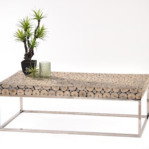 Könnte beinhalten: Rechteckiger Couchtisch mit einer Oberfläche aus kleinen, hellfarbigen Holzrundungen. Der Tisch hat ein silbernes Metallgestell und eine kleine Topfpflanze und einen Kerzenhalter. Der Tisch ist etwa 122 cm lang.