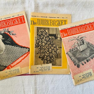 May include: Three vintage issues of "The Workbasket" magazine are displayed, featuring covers in red and yellow with illustrations of crochet projects. The magazines are from 1961, with the text "The Workbasket" prominently displayed.