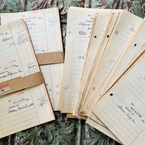 May include: A collection of aged ledger sheets with handwritten entries and brown paper tape. The papers are yellowed with age, and some have hole punches along the left edge. The handwriting is in black ink.