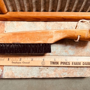 May include: A wooden brush with black bristles and a light brown handle. A wooden ruler with the text "TWIN PINES FARM DAIRY" is next to the brush. The brush is approximately 7 inches long.