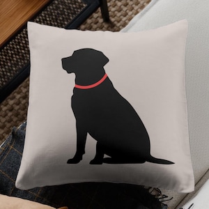 May include: A beige throw pillow with a black silhouette of a dog sitting with a red collar.