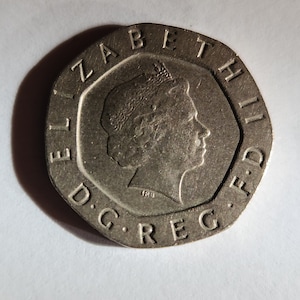 Może przedstawiać: Srebrna moneta z profilem królowej Elżbiety II po jednej stronie. Na monecie widnieje napis "ELIZABETH II D.G. REG. F.D." wokół krawędzi.