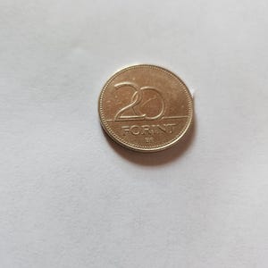 May include: A gold-colored 20 Forint coin. The coin features the number 20 in a large font above the word "FORINT". The coin has a textured edge and is set against a white background.