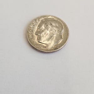 Könnte beinhalten: Eine silberne US-Dime-Münze mit dem Profil von Präsident Franklin D. Roosevelt auf der Vorderseite. Die Münze trägt die Inschriften "LIBERTY" und "IN GOD WE TRUST".