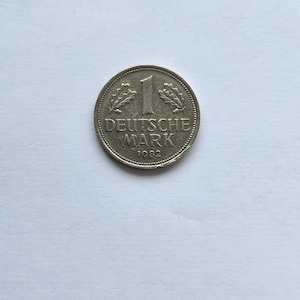 Puede incluir: Una moneda de 1 Deutsche Mark de plata de 1982. La moneda presenta el texto "DEUTSCHE MARK" y el número "1" en el centro, con hojas de roble a ambos lados. El año "1982" está en la parte inferior.