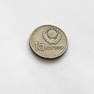 Può includere: Una moneta d'argento con la scritta "15 KOПEEK" e un emblema dettagliato con una stella, grano e una falce e martello. La moneta è circolare con un bordo zigrinato.