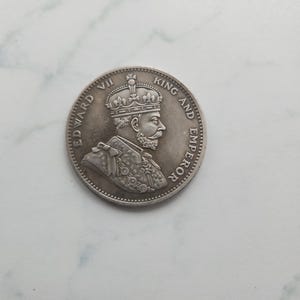 May include: Silver coin depicting a profile portrait of King Edward VII, wearing a crown. The inscription reads "EDWARD VII KING AND EMPEROR".