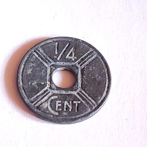 Puede incluir: Una moneda de metal de color plateado con la inscripción "1/4 CENT" y un diseño de cuatro líneas que irradian desde el centro.