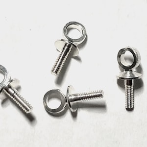 May include: Close-up of four silver-colored eye bolt screws. Each screw has a threaded shaft, a flat washer, and a circular eyelet. The eyelets are designed for attaching cords or other hardware. The bolts are arranged on a white surface.