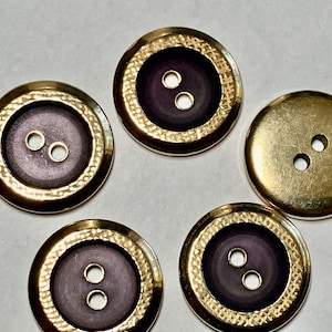 May include: Five gold-colored buttons with a textured, hammered-metal effect around the edges. The centers are a deep purple color, each with two small holes for sewing. One button is solid gold.