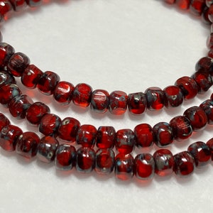 May include: Strands of red and black glass beads. The beads are small, cylindrical, and have a mottled appearance. The beads are strung together, creating a necklace or bracelet.