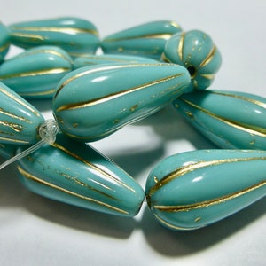 May include: A strand of turquoise blue glass beads with gold accents. The beads are shaped like teardrops and have a textured surface.