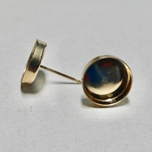 May include: Two gold-toned earring settings with a round, flat base and a post for attaching to an earring.