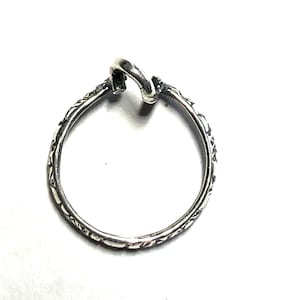May include: A silver ring with an ornate design. The ring features a looped top and a detailed pattern around the band. The ring is set against a white background, highlighting its intricate details and craftsmanship.