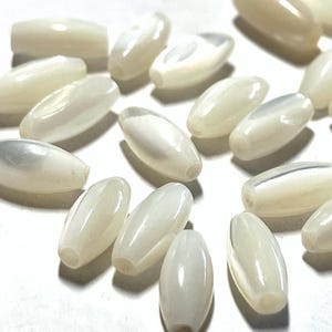 May include: A collection of small, elongated, oval-shaped beads with a smooth, iridescent white finish. Each bead features a central hole running through its length, displaying a pearlescent sheen and a polished surface texture throughout.
