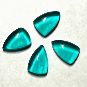 May include: Four teal-coloured, triangular gemstones arranged in a circular pattern. Each gem has a smooth, polished surface and a slightly rounded shape. The gems are a vibrant, translucent teal colour.