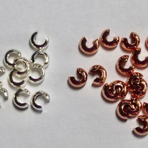 May include: A collection of silver and copper-colored C-shaped crimp beads. The beads are small, with a smooth, rounded appearance. They are used in jewelry making to secure clasps and other components.