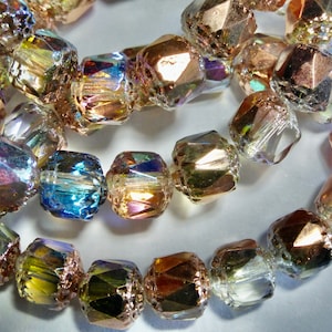 May include: Strands of faceted, iridescent beads in shades of gold, bronze, and blue. The beads have a geometric shape and are strung together with a thin, clear cord. These beads are suitable for jewelry making.