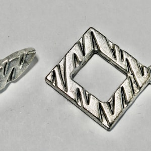 May include: Silver-toned jewelry clasp set. The set includes a diamond-shaped clasp with a textured, zig-zag pattern and a matching curved bar. The diamond clasp has a small loop for attachment. Ideal for jewelry making.
