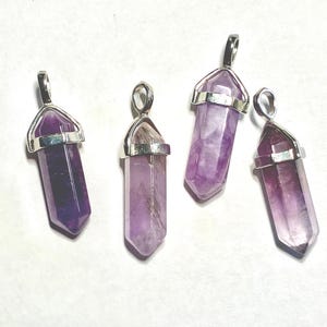 May include: Four amethyst crystal pendants with silver-colored metal caps and loops. The crystals vary in shades of purple, from deep violet to pale lavender. Each pendant is a hexagonal prism shape.