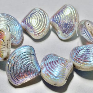 May include: A strand of iridescent glass beads shaped like seashells. The beads are a light blue color with a pearlescent finish.