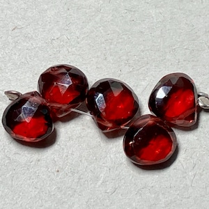 May include: Five faceted red gemstone beads strung on a thin wire. The beads are all the same size and shape, and they have a glossy finish.