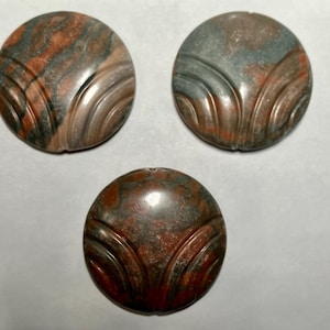 May include: Three round, carved, brown and green stone buttons with a decorative pattern.