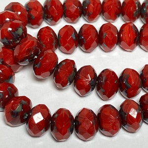 May include: A strand of red glass beads with a faceted, oval shape. The beads have a mottled, marbled appearance with hints of black and white.