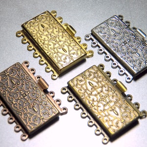 May include: Three metal clasps with ornate designs in gold, silver, and bronze. Each clasp has multiple loops for attaching jewelry.