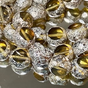 May include: A strand of round, faceted glass beads with a crackled, white and brown finish. The beads are translucent and have a golden yellow hue.