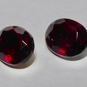 May include: Two oval-shaped, dark red gemstones with a faceted cut.