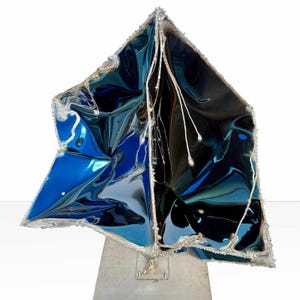 May include: Abstract sculpture with a triangular shape, featuring a mix of glossy blue and black surfaces. The edges are outlined with silver trim, and it stands on a silver base. White string-like elements with silver droplets hang from the top.