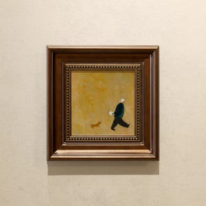 Può includere: Opera d'arte incorniciata raffigurante una persona che porta a spasso un cane. La persona indossa una giacca e pantaloni scuri, con un cappello bianco. Il cane è piccolo e marrone. Lo sfondo è giallo-beige.