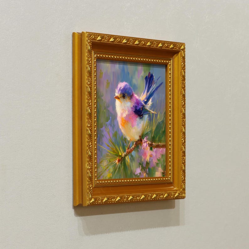 Puede incluir: Pintura al &oacute;leo enmarcada de un peque&ntilde;o p&aacute;jaro con plumas azules, moradas, rosas y blancas posado en una rama. La pintura est&aacute; en un marco dorado adornado, con un fondo de colores suaves.