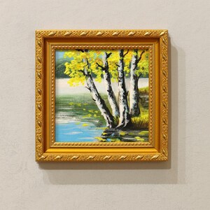 Op de afbeelding: Een ingelijst landschapsschilderij met berken met gele bladeren naast een blauw meer. Het kunstwerk zit in een goudkleurige, sierlijke lijst. De schildering toont een serene buitensc&egrave;ne.