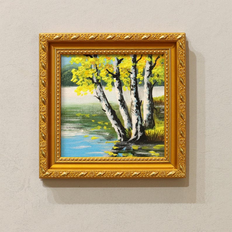 Op de afbeelding: Een ingelijst landschapsschilderij met berken met gele bladeren naast een blauw meer. Het kunstwerk zit in een goudkleurige, sierlijke lijst. De schildering toont een serene buitensc&egrave;ne.
